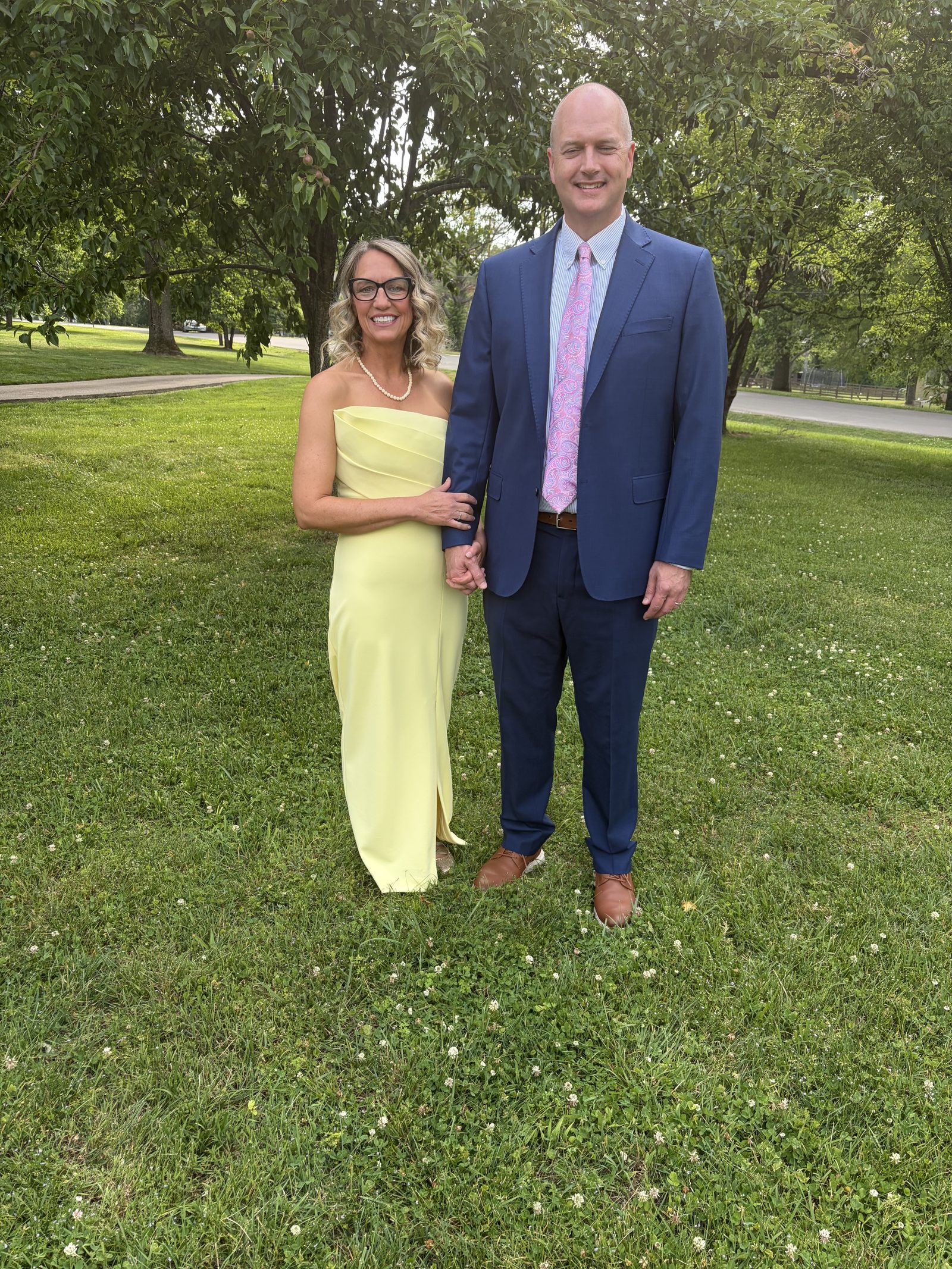 Client in a pale yellow strapless gown beside her partner in a navy suit, outdoors before an event